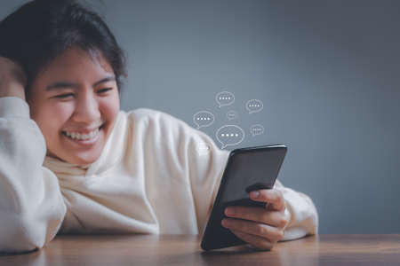 Happy asian woman chatting social media interactions on mobile phone with notification icons of message. internet digital marketing concept.の写真素材