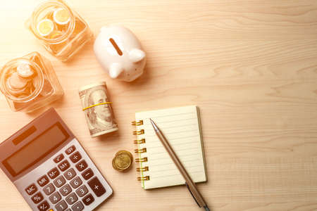 Piggy bank, calculator, dollar bill, glass jar filled with coins, notebook and pen, depict budget planning for basic needs, family,personal expense, Business and personal financial concept.の写真素材