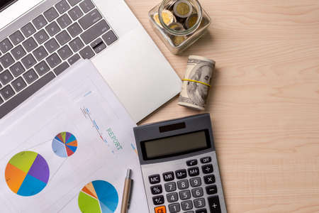 Calculator with a glass jar filled with coins, computer laptop, dollar bills, graph of investment with business stuff for saving money, with space for text. Business and personal financial concept.の写真素材
