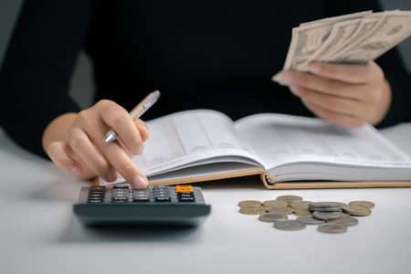 Woman using calculator with pen in her hand and hold dollar bill for calculating financial expense at home office, financial accounting calculate money payments manage expenses.の写真素材