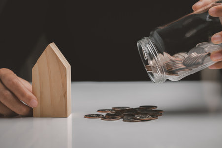 Woman holding house model and poured a coin from a glass jar, Property investment and house mortgage financial concept.の写真素材