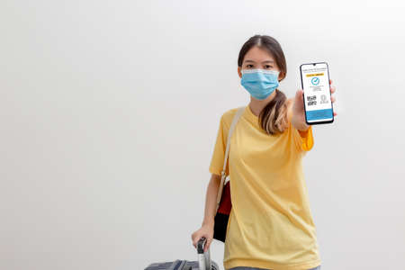 Vaccine passport, Woman wearing mask and holding smartphone showing health passport of vaccination certification, status proof immunized against COVID-19 for travel during covid-19 pandemic.の写真素材