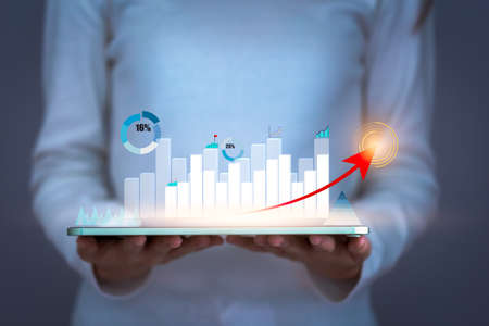 Business woman holding tablet and showing business growing virtual screen of statistics,  red arrow up with graph and chart , strategy and planning concept.の写真素材