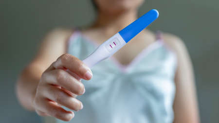 Positive pregnancy test on a woman's hand in pajamas.