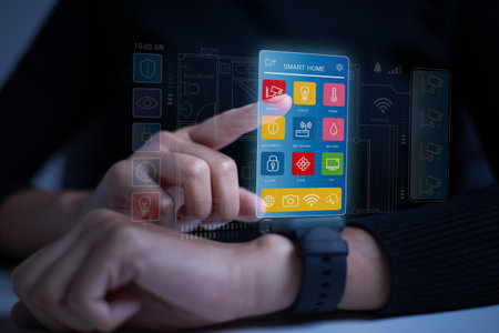 Close-up shot of a hand holding a smartwatch, fingers resting on the screen. The screen displays colorful icons representing various smart home devices. Internet of thing concept.の写真素材