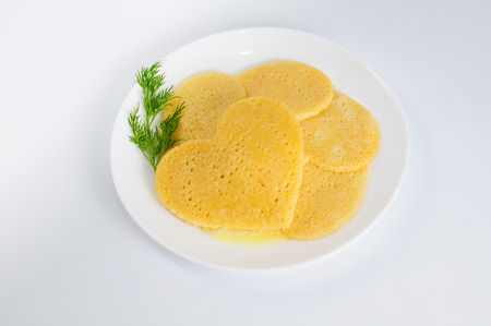 Several pancakes in the shape of a heart on white plate with sprig of dillの写真素材