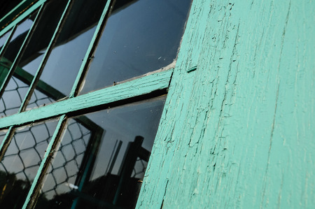 Old window with unwashed windowpane and chapped window frame covered with cracked green paint  and rusty nails close viewの写真素材