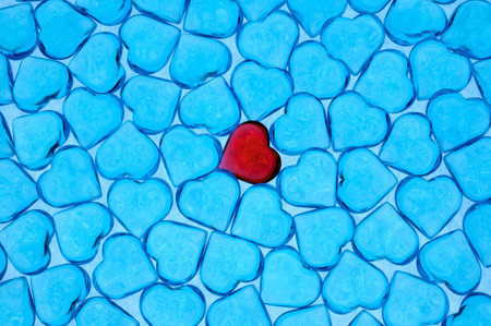 Background of little blue plastic hearts with one red located on centerの写真素材