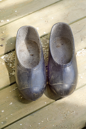 a pair of dirty old black rubber galoshes on a wooden floor green color in the daytimeの写真素材