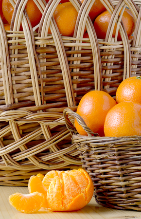 pile of tangerines in a small and a large basket and have not been fully cleansed with the Mandarin slices on the table in the background of a wicker basketの写真素材