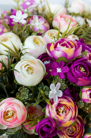 Still life with artificial flowers of roses and carnations in red, purple, yellow and white and green petals. The image is vertical, close-up.の写真素材
