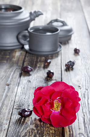 Oriental tea set of teapot and mugs of black ceramic with tea fruits and rose hip flowers on a brown wooden table in the countryside indoors close-up. Side view.の写真素材