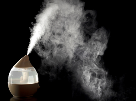 White steam produces home ultrasonic humidifier round made of plastic transparent material. Shooting is done in a low key.の写真素材