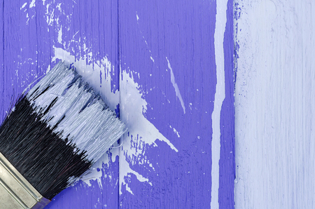 The background of the wooden boards is painted part white and honor purple paint brush bristles close-up.の写真素材