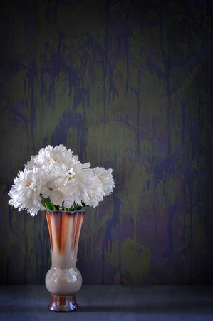 A bouquet of white peonies in a ceramic brown vase on a gray table and dark blue background.の写真素材