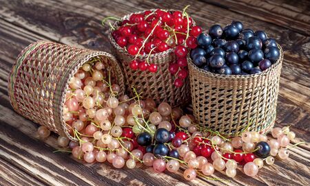 Three serving baskets with red, white, and black currant berries. Scattered on a wooden table. On a wooden background close-up.の写真素材