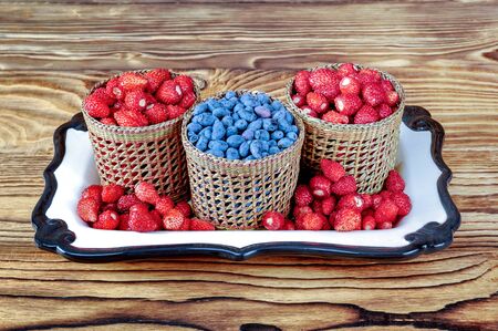 Three serving baskets of strawberries and blueberries. On a white ceramic tray on a wooden table close-up.の写真素材
