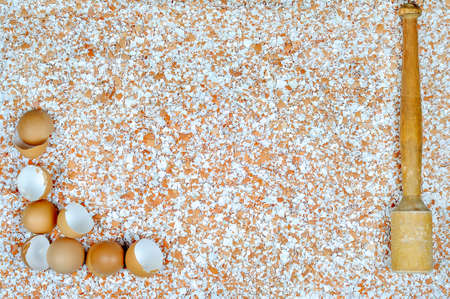 A broken eggshell on a table and a wooden mortar in the opposite place in the picture against the...