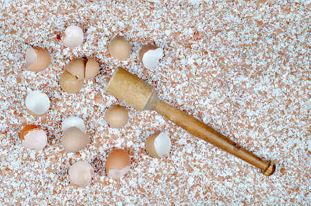 Broken eggshells scattered on the table, wooden mortar on the background of crushed eggshells.