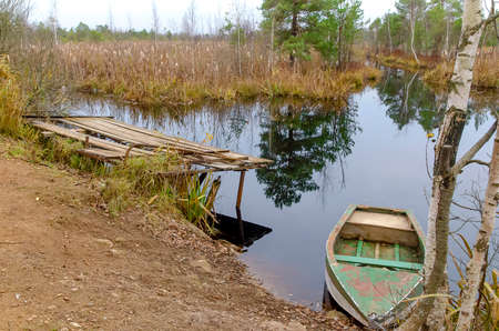Vintage small metal fishing boat without oars stands at the shore of the reservoir tied to a tree...