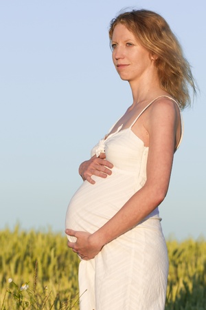 pregnant woman in white dress relaxing outdoorsの写真素材