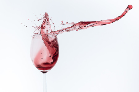 red wine splashing out of a glass, isolated on whiteの写真素材