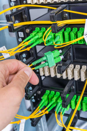 Hand of computer technician connecting fiber optics cable into data switch