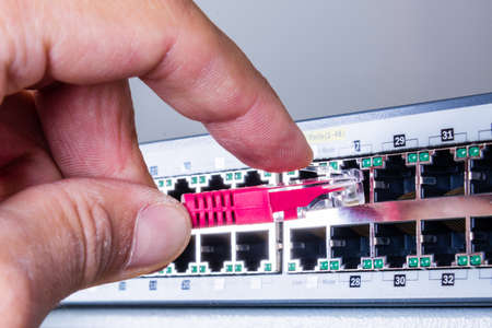 hand of administrator plugging in red patch cable into empty switchboard
