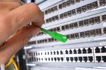 hand of administrator plugging in fiber optic cable into empty switchboard