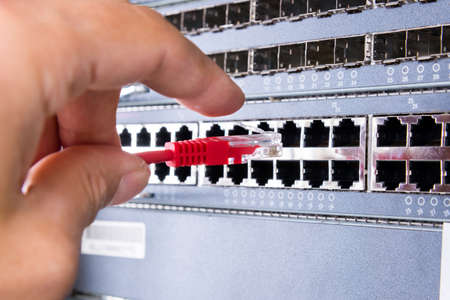 hand of administrator plugging in red patch cable into empty switchboard