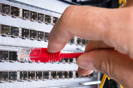 hand of administrator plugging in red patch cable into empty switchboard