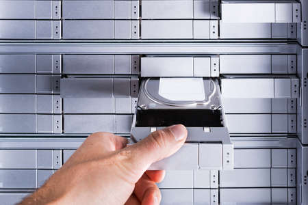 close-up on a hand of an IT administrator inserting hard drive into data storage arrayの写真素材