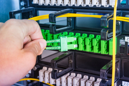 Hand of computer technician connecting fiber optics cable into data switch