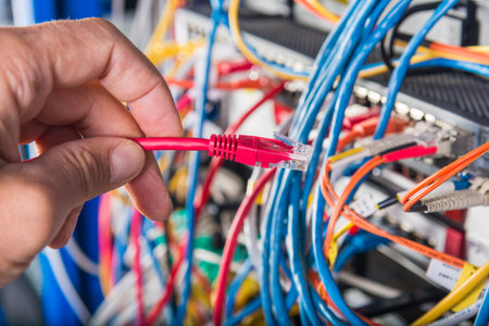 closeup of hand of administrator connecting network cable into switch