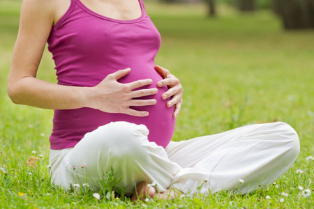 Pregnant woman relaxing in the park, hands holding the belly.の写真素材