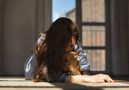 young girl and her dog french bulldog are playing on the floor of their apartmentの写真素材