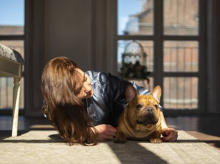 young girl and her dog french bulldog are playing on the floor of their apartmentの写真素材