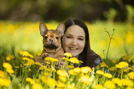 young woman and a french bulldog puppy are resting in a parkの写真素材