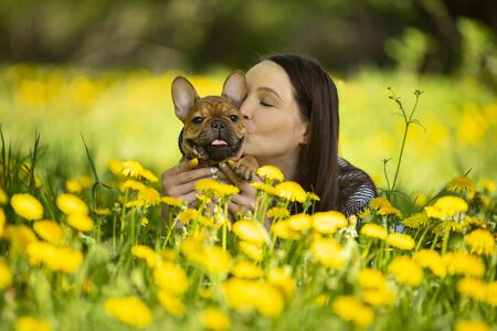 young woman and a french bulldog puppy are resting in a parkの写真素材