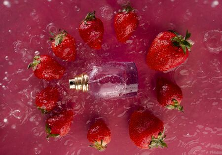 fashionable perfume bottle and ripe juicy strawberries in spray of waterの写真素材