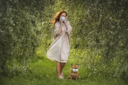 young woman and her dog french bulldog walk in the park in medical masks. New normalの写真素材