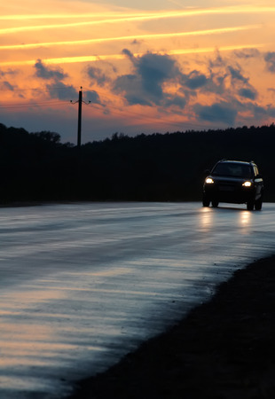 Car driving on a late evening against a sky with some cloudsの写真素材