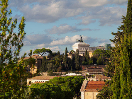 Majestic Vittorio Emanuele monument in Rome, Italy, seen behind dense roofs and treesの写真素材