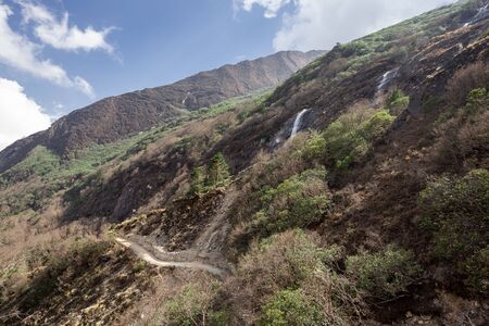 Landscape in Nepal Himalayas, narrow path winding below cascaded waterfallsの写真素材
