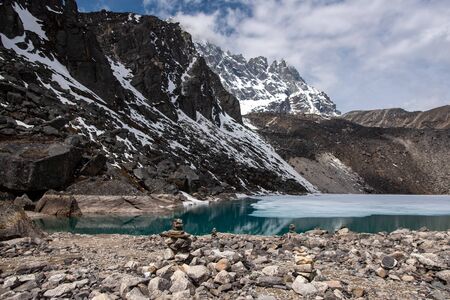 Traditional Nepalese stone pyramid on shore of Gokyo lake, with snow govered mountian slopes behindの写真素材