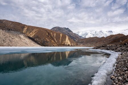 Thin layer of ice on scenic Gokyo lake in Nepal Himalayas, with shite snow covered mountain range in far distanceの写真素材