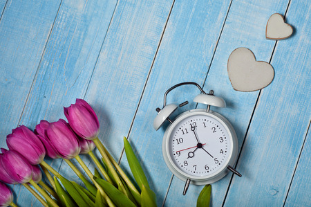 Bouquet of Tulips with vintage alarm clock and a wooden heart on a blue wooden background. Top view. Copy spaceの写真素材