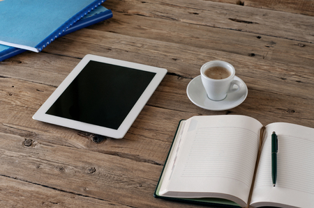 White tablet computer with a blank screen on the wooden table with a cup of black coffee and notepad.の写真素材