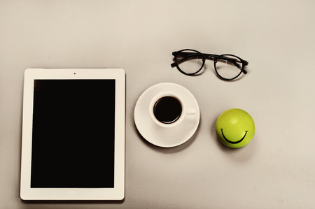 White tablet computer with a cup of coffee and glasses on a gray surface. Top view