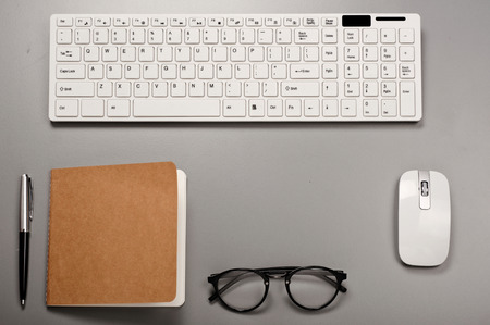 Office workstation with a keyboard, notebook, pen and glasses.